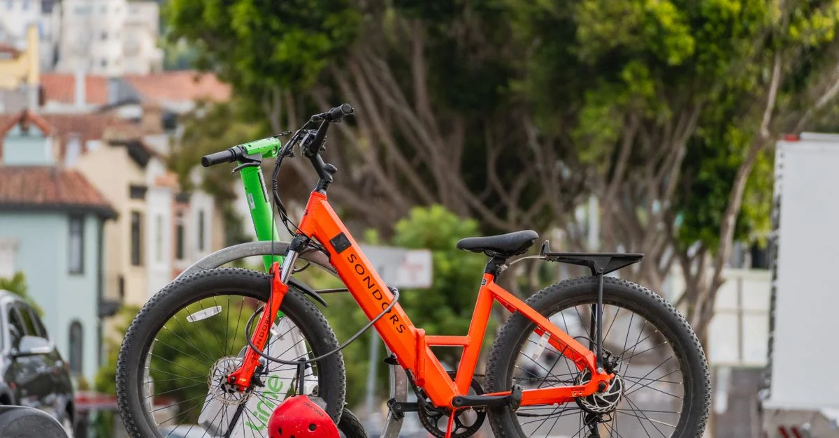 Vélos électriques vibrants stationnés à l'extérieur dans une scène urbaine avec des arbres en arrière-plan.