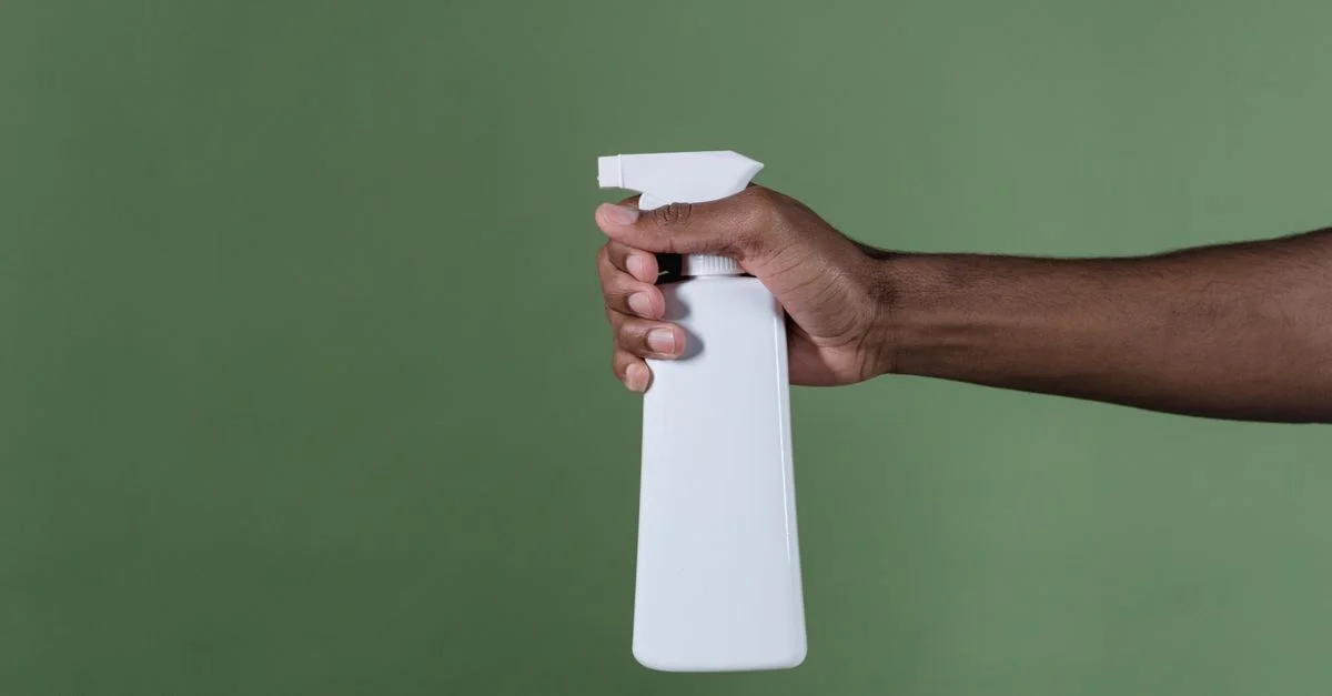 Une main tient un flacon vaporisateur blanc sur un fond vert, parfait pour des concepts de produits de nettoyage.