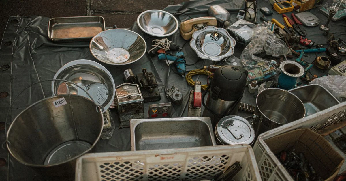Divers objets en métal et outils vintage exposés dans un marché aux puces en plein air sur asphalte.