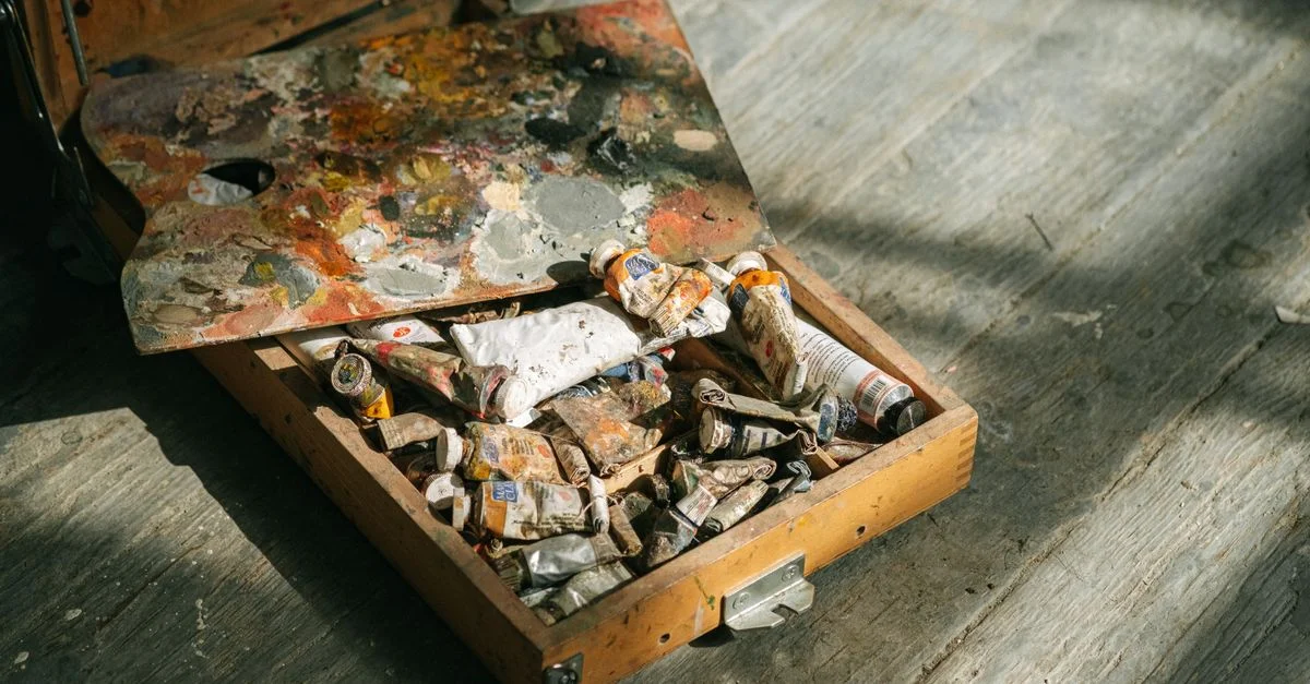 Gros plan d'un ensemble de peinture en bois avec des tubes colorés et une palette sur un sol texturé.