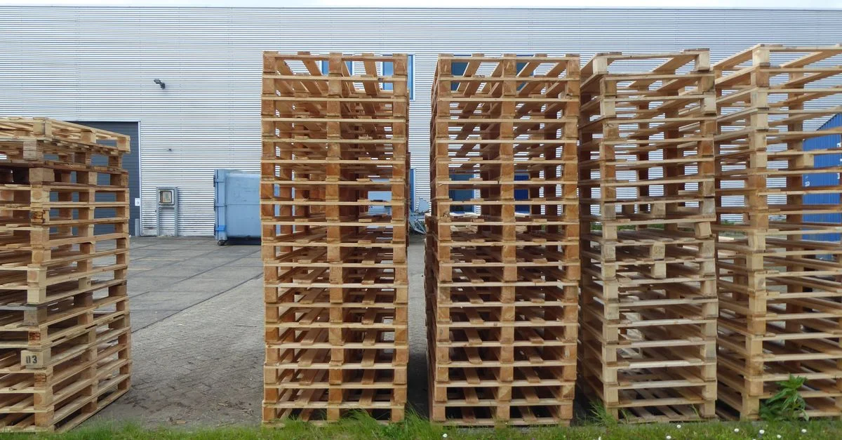 Rangées de palettes en bois empilées à l'extérieur près d'un entrepôt, parfaites pour des thèmes industriels et logistiques.